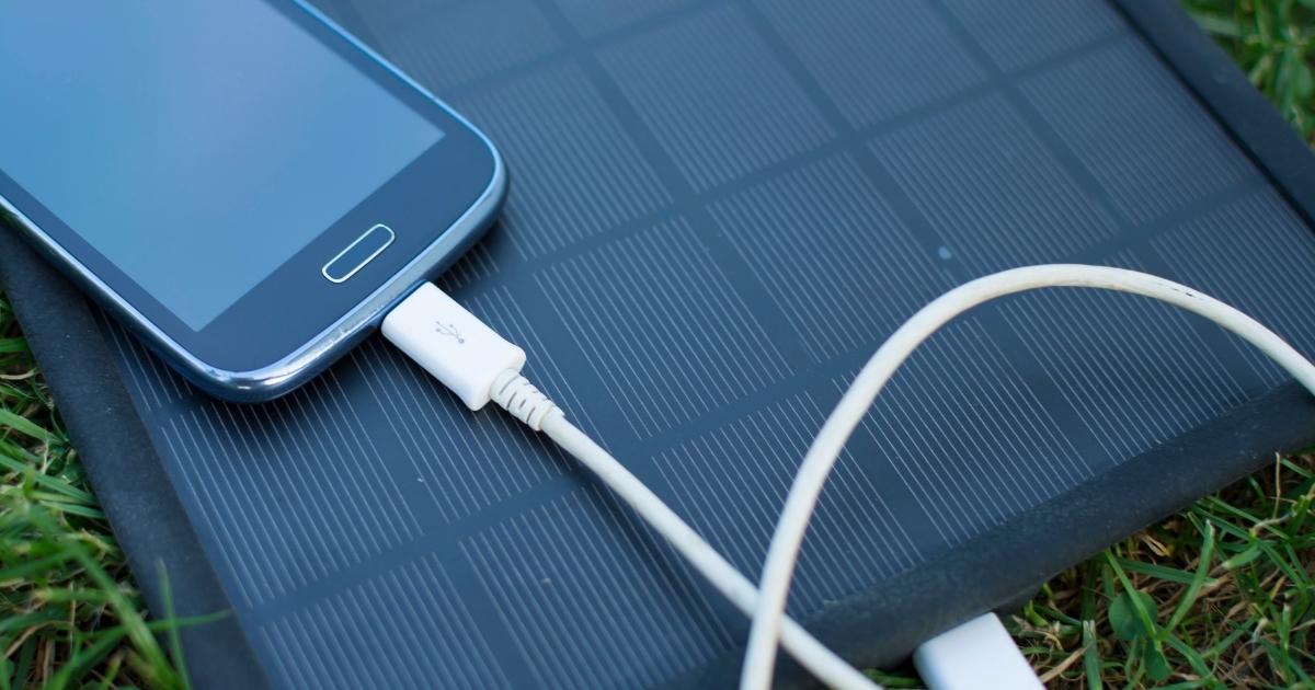 Telefon ładowany przez ładowarkę solarną. Leżą na zielonej trawie.