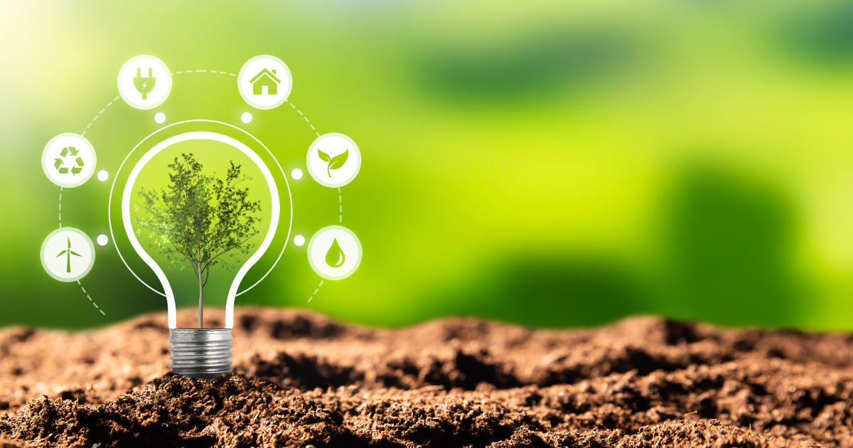 Z ziemi wyrasta drzewko otoczone żarówką, wokół żarówki znajduje się pięć ikon symbolizujących źródła energii odnawialnej. W tle intensywna zieleń.